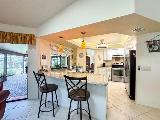 Kitchen featuring kitchen peninsula, a kitchen bar, stainless steel appliances, a tray ceiling, and white cabinets