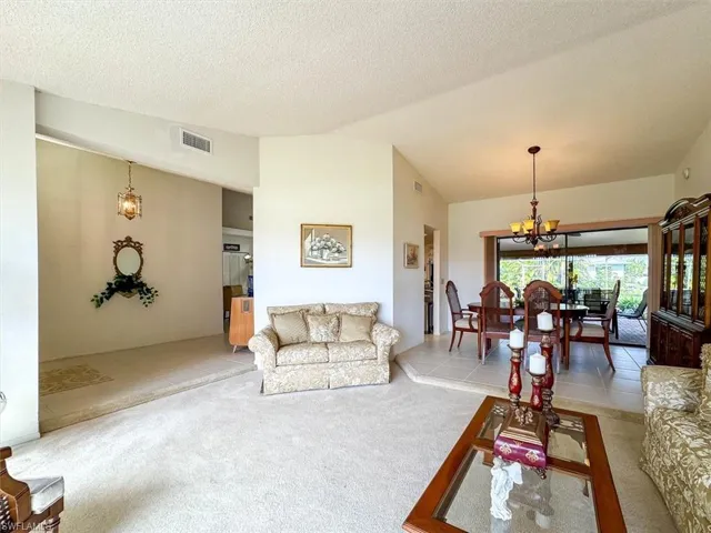 Carpeted living room featuring a textured ceiling, vaulted ceiling, and an inviting chandelier