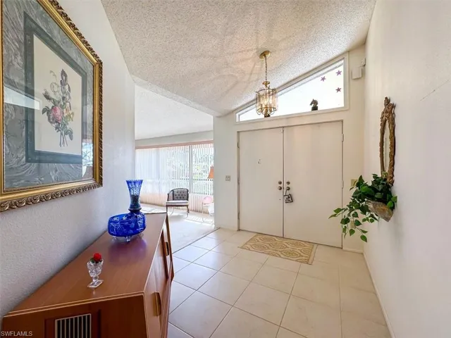 Tiled entrance foyer featuring lofted ceiling, a textured ceiling, and an inviting chandelier