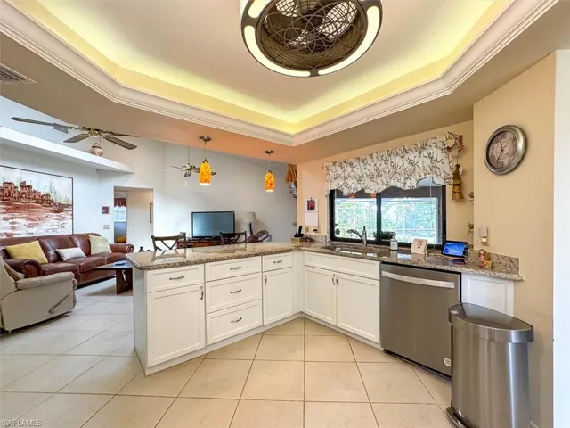 Kitchen with white cabinets, a raised ceiling, sink, stone countertops, and dishwasher