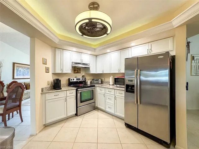 Kitchen with light stone countertops, white cabinetry, stainless steel appliances, and ornamental molding