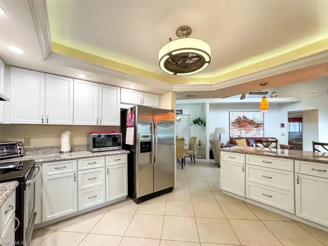 Kitchen with white cabinets, stainless steel appliances, a raised ceiling, and light stone counters
