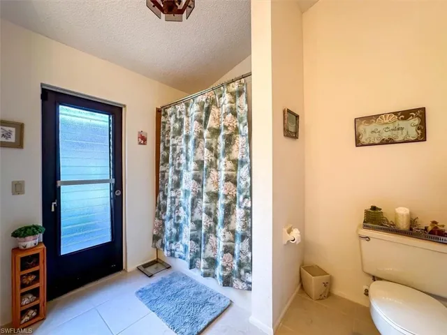 Bathroom with tile patterned floors, toilet, a textured ceiling, and walk in shower