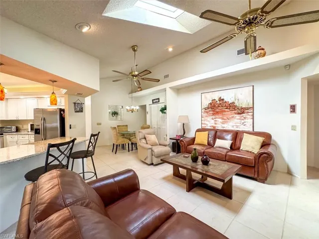 Living room featuring ceiling fan with notable chandelier, a skylight, a towering ceiling, a textured ceiling, and light tile patterned flooring