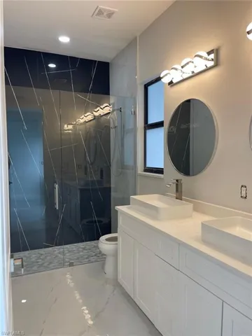 Bathroom with toilet, a shower with door, tile patterned flooring, and double sink vanity
