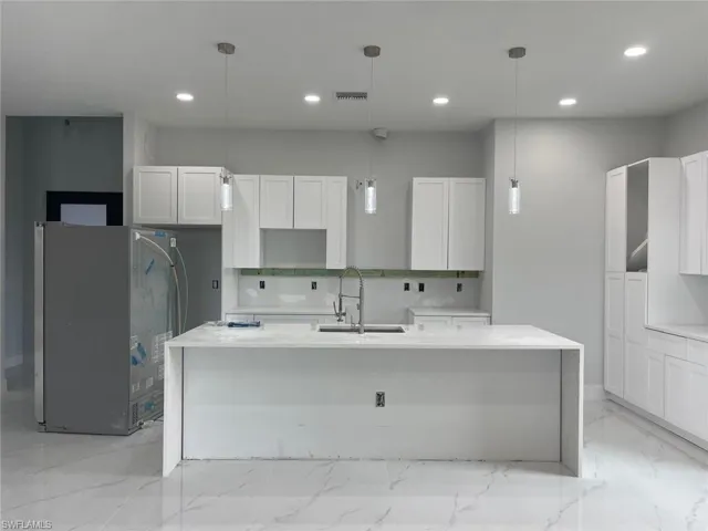 Kitchen with light tile patterned flooring, tasteful backsplash, white cabinets, sink, and a center island with sink