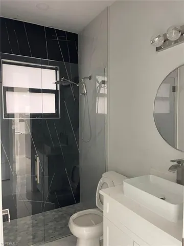 Bathroom with a shower with shower door, vanity, and toilet