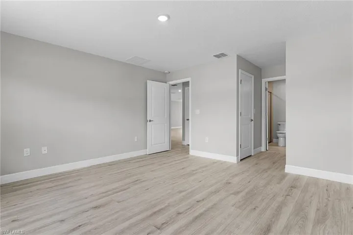 Unfurnished bedroom with light wood-style floors, baseboards, recessed lighting, and connected bathroom