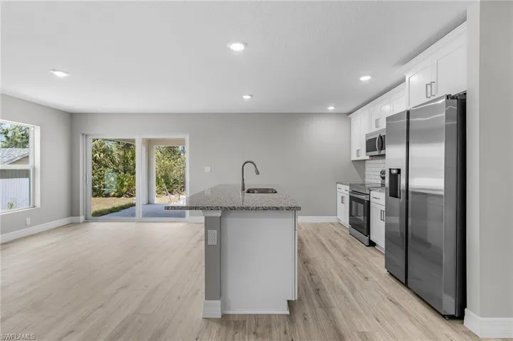 Kitchen with stainless steel appliances, a sink, a center island with sink, stone countertops, and light wood-style floors