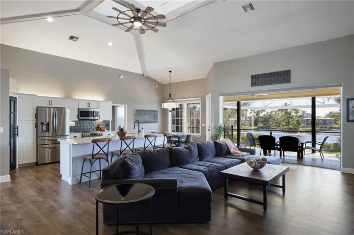 Living room featuring high vaulted ceiling, ceiling fan, dark wood-style floors, and a sunroom