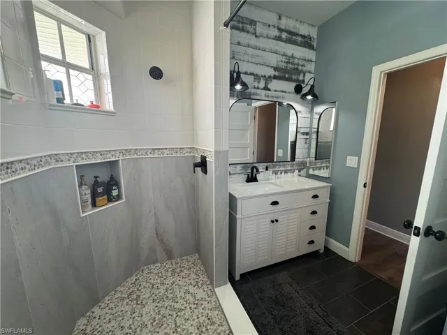 Bathroom with dark tile patterned flooring, tiled shower, vanity, and decorative backsplash