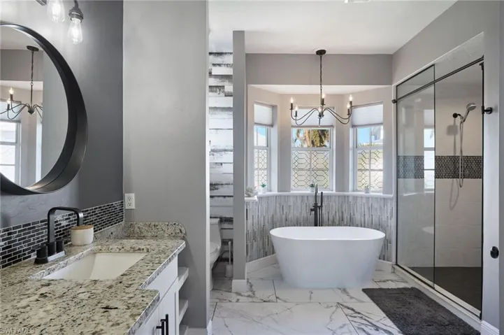Bathroom with a chandelier, a soaking tub, a stall shower, vanity, and light marble finish flooring