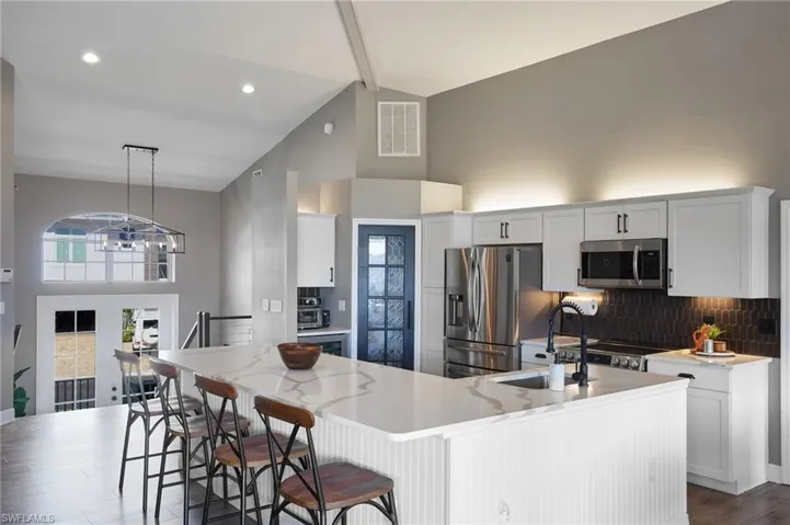 Kitchen with high vaulted ceiling, beamed ceiling, white cabinets, stainless steel appliances, and tasteful backsplash