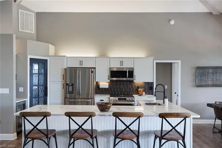Kitchen with appliances with stainless steel finishes, an island with sink, white cabinetry, beamed ceiling, and light stone counters