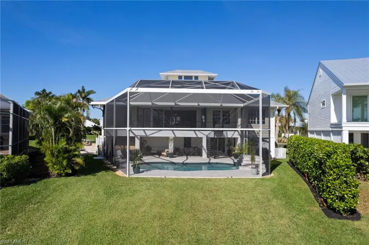 Back of property with a lanai, a lawn, an outdoor pool