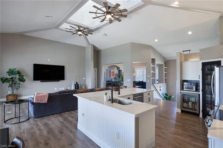 Kitchen with a ceiling fan, open floor plan, white cabinets, a skylight, and high vaulted ceiling