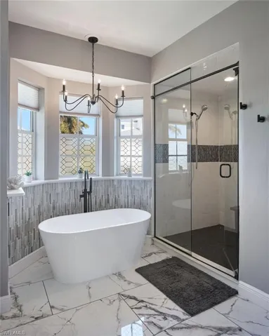 Full bath featuring a soaking tub, a wainscoted wall, a shower stall, light marble finish floors, and a chandelier