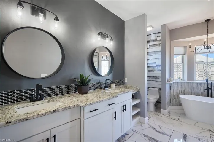 Full bathroom with a soaking tub, double vanity, light marble finish flooring, and a chandelier