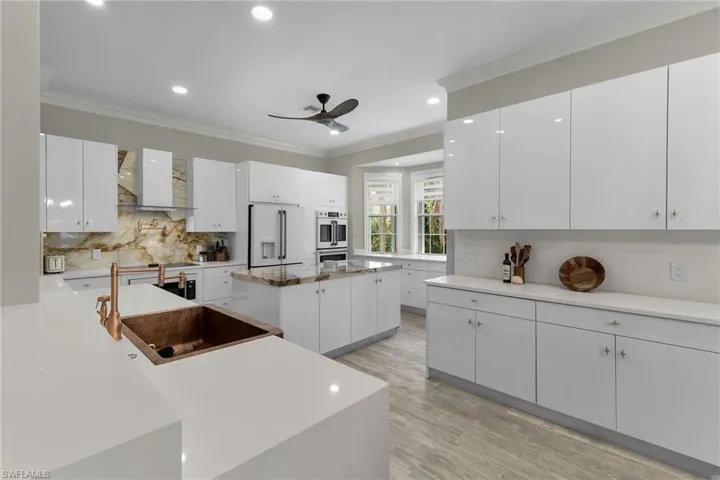 Kitchen with white refrigerator with ice dispenser, wall chimney exhaust hood, ceiling fan, tasteful backsplash, and recessed lighting