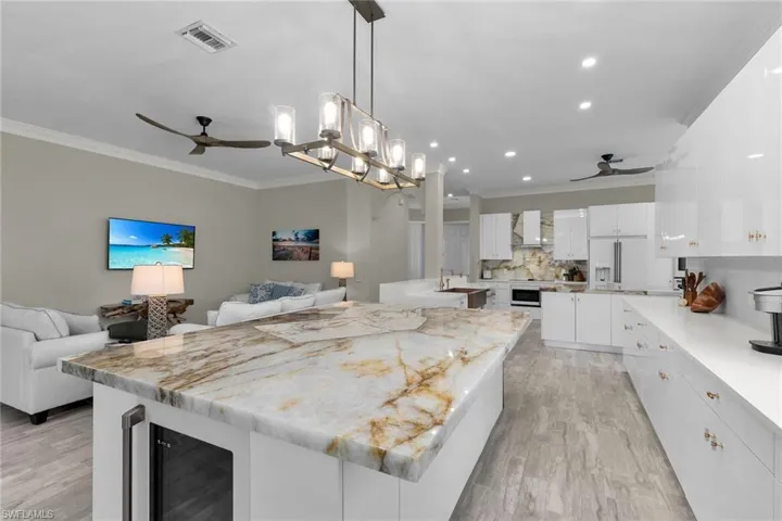 Kitchen with a ceiling fan, beverage cooler, wall chimney exhaust hood, open floor plan, and crown molding
