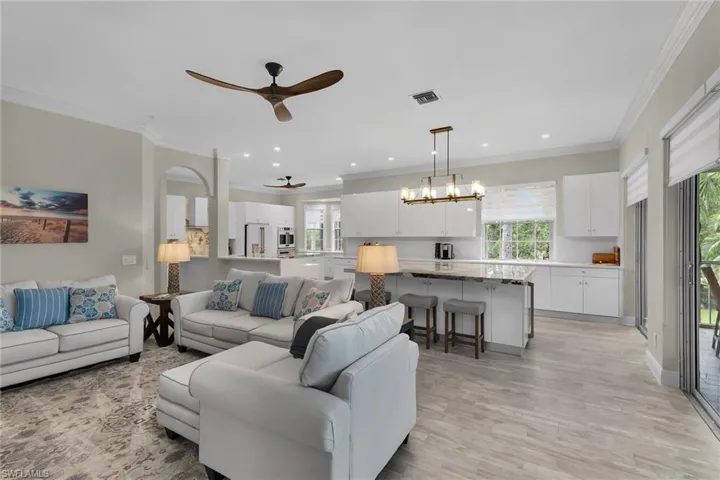 Living area featuring ceiling fan, plenty of natural light, light wood finished floors, a chandelier, and crown molding