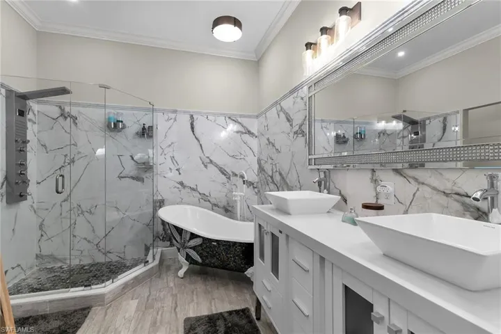 Bathroom featuring tile walls, a freestanding tub, a marble finish shower, double vanity, and ornamental molding
