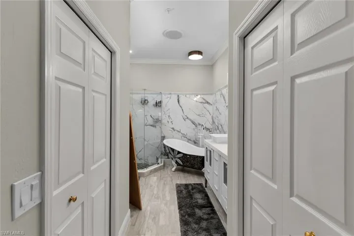 Bathroom featuring a marble finish shower, crown molding, tile walls, vanity, and wood finished floors