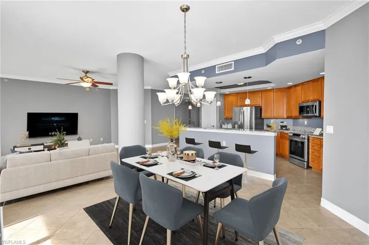 Dining space with crown molding, a ceiling fan, a chandelier, and light tile flooring