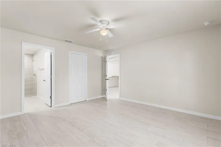 Spacious room featuring wood-finish tile flooring, neutral wall tones, and a ceiling fan with integrated lighting