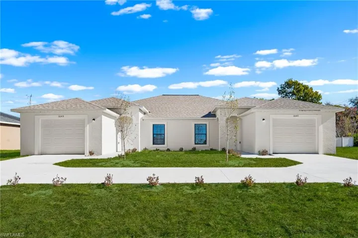 Duplex residence featuring stucco exterior, individual garage access for each unit, and a shared, curved concrete driveway