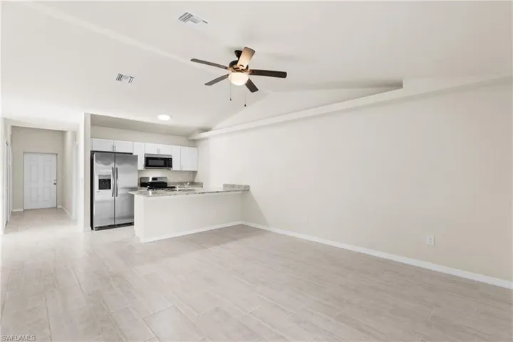 Open-concept living space with light-toned tile flooring, vaulted ceilings, and a ceiling fan