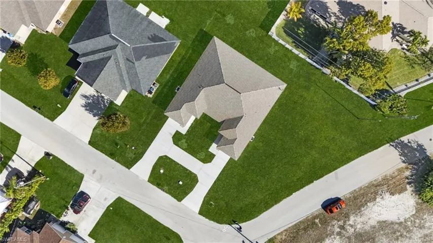 Aerial view showcasing a property with a large, L-shaped concrete driveway