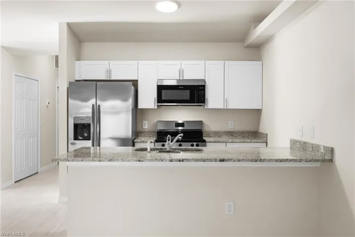 Open-concept kitchen featuring white cabinetry, stainless steel appliances, a double basin sink, and a spacious breakfast bar with stone countertops