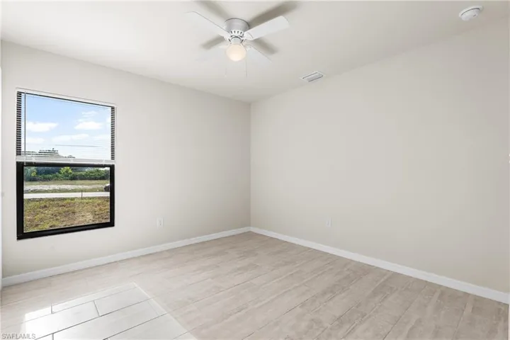 Spacious room featuring wood-finish tile flooring, a large window with horizontal blinds, and a ceiling fan with integrated lighting