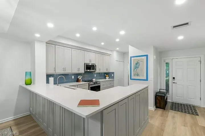 Kitchen with appliances with stainless steel finishes, light wood-style floors, light countertops, tasteful backsplash, and a peninsula