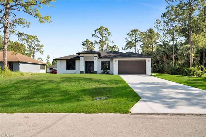 Prairie-style house featuring stucco siding, an attached garage, a front lawn, and driveway