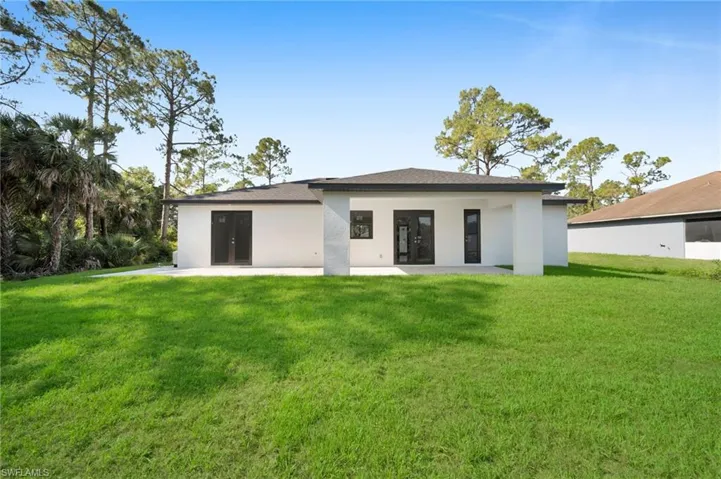 Rear view of house with a lawn, stucco siding, and a patio area