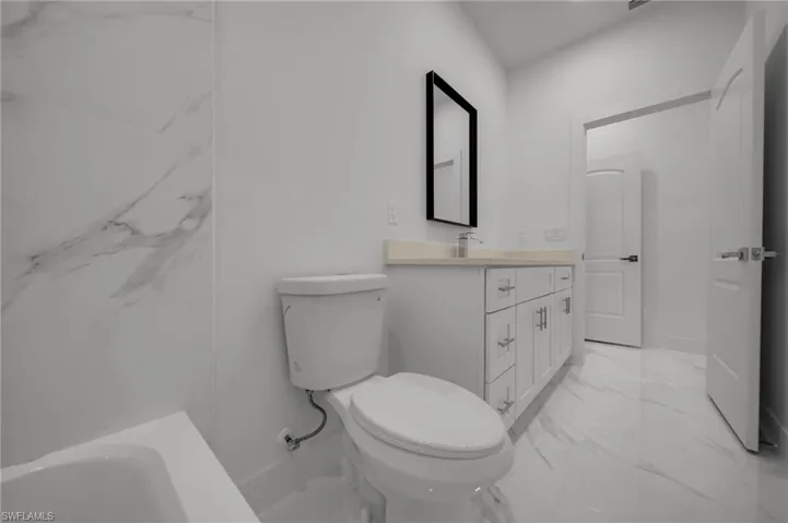 Full bath with marble look tiles, toilet, vanity, and a tub to relax in
