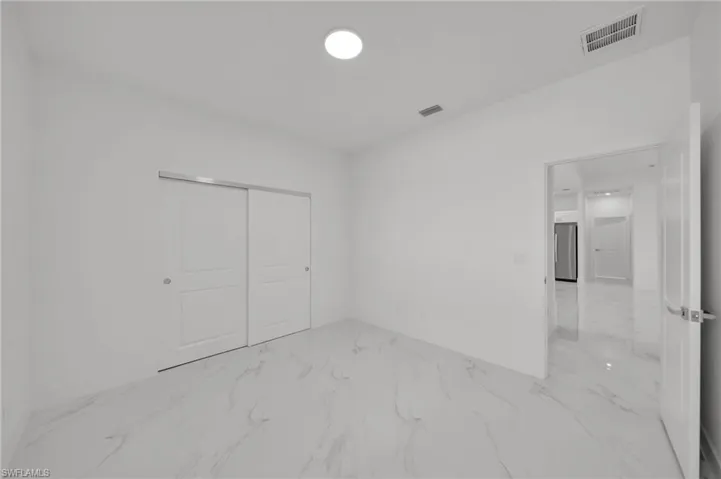 Unfurnished bedroom featuring light marble finish flooring, baseboards, a closet, and freestanding refrigerator