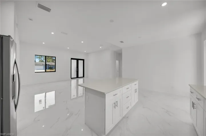 Kitchen featuring stainless steel refrigerator with ice dispenser, recessed lighting, white cabinets, light marble finish flooring, and a center island