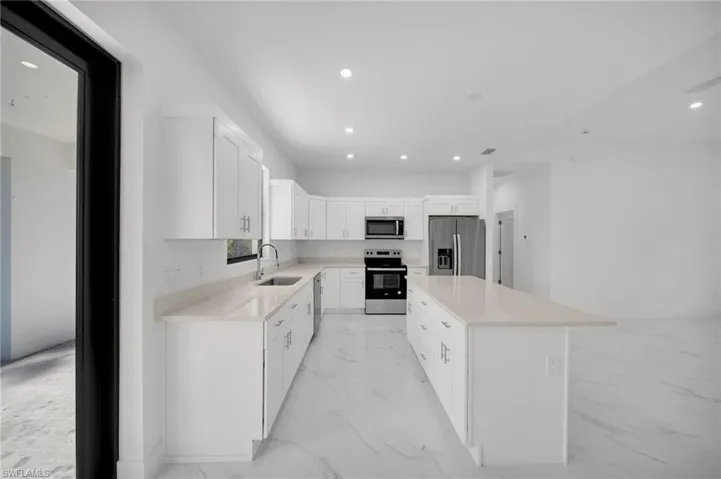 Kitchen featuring stainless steel appliances, light marble finish flooring, a sink, a center island, and recessed lighting
