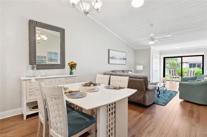 Dining space featuring ceiling fan with notable chandelier, vaulted ceiling, ornamental molding, and wood-type flooring
