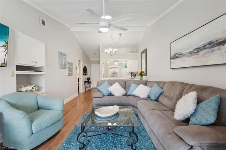 Living room with crown molding, ceiling fan with notable chandelier, light wood-type flooring, and lofted ceiling with beams