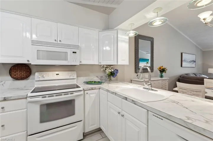 Kitchen with white cabinetry, vaulted ceiling, white appliances, and sink