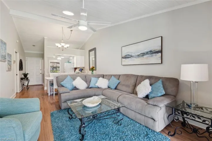 Living room with vaulted ceiling, ceiling fan with notable chandelier, wood ceiling, crown molding, and hardwood / wood-style flooring