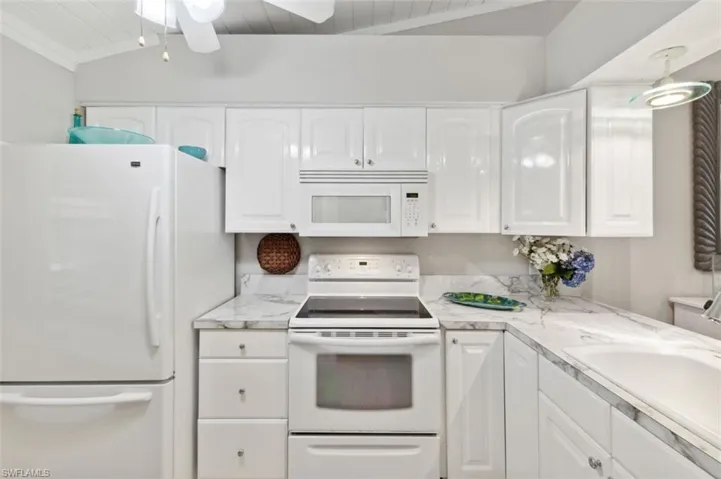 Kitchen with light stone countertops, white appliances, lofted ceiling with beams, ceiling fan, and white cabinets