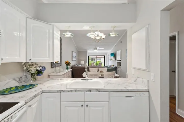 Kitchen featuring ceiling fan with notable chandelier, white appliances, kitchen peninsula, sink, and white cabinetry