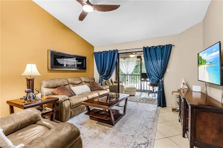 Living room with a ceiling fan, vaulted ceiling, and light tile patterned floors