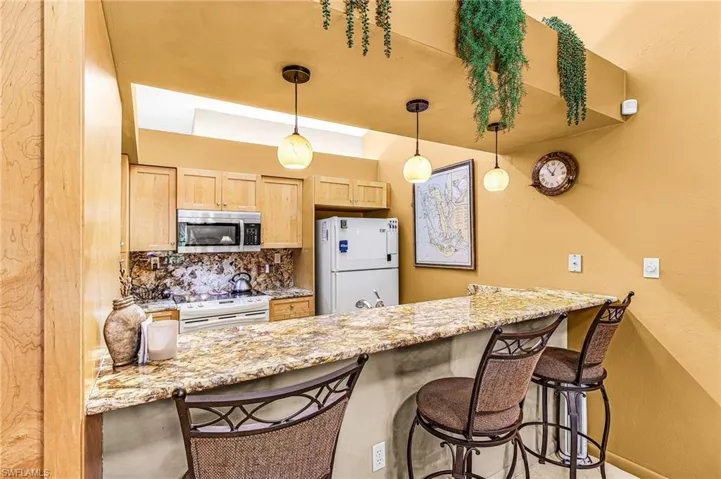 Kitchen featuring a breakfast bar, light stone countertops, white appliances, and light brown cabinets