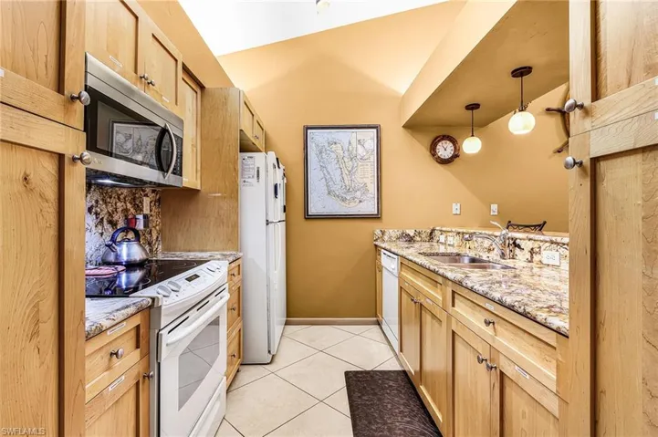 Kitchen with white appliances, light stone countertops, decorative light fixtures, light tile patterned floors, and decorative backsplash